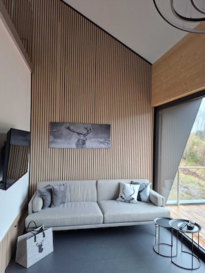 Uma sala de estar moderna com um sofá, almofadas, uma TV de tela plana e uma janela grande.