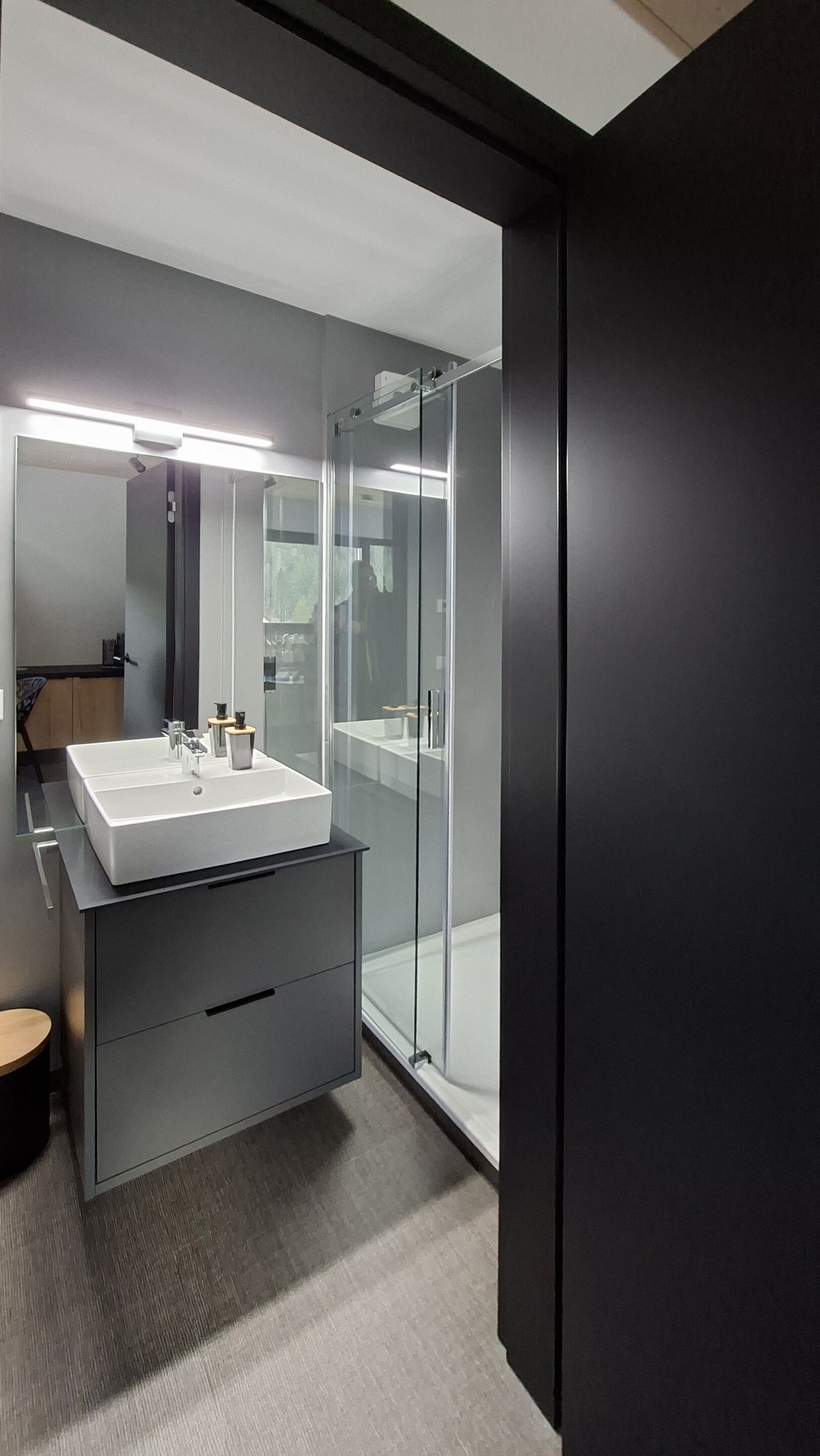 Une salle de bain moderne avec un grand miroir, un lavabo blanc et une cabine de douche en verre.