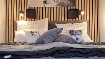 A bedroom with a bed, pillows, a wall-mounted picture, and two wall-mounted speakers.