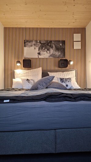 A bedroom with a bed, pillows, a wall-mounted picture, and two wall-mounted speakers.