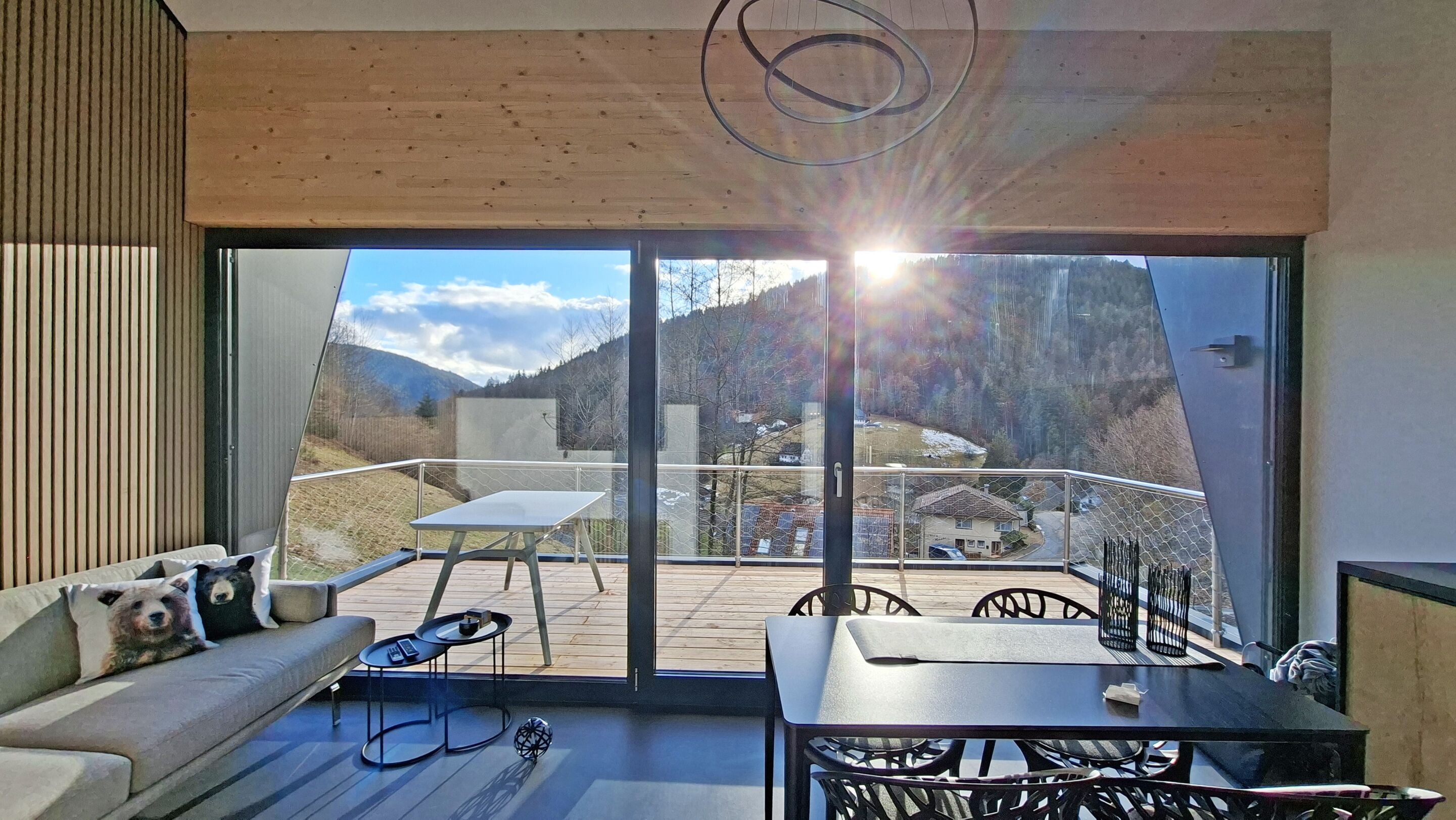 A modern interior with a balcony, a sofa, a table, and a view of a mountainous landscape.