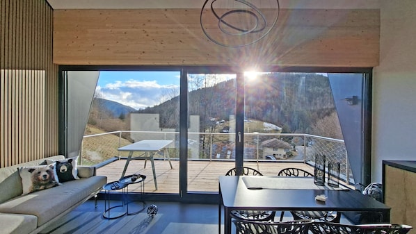 Un interior moderno con un balcón, un sofá, una mesa y vistas a un paisaje montañoso.