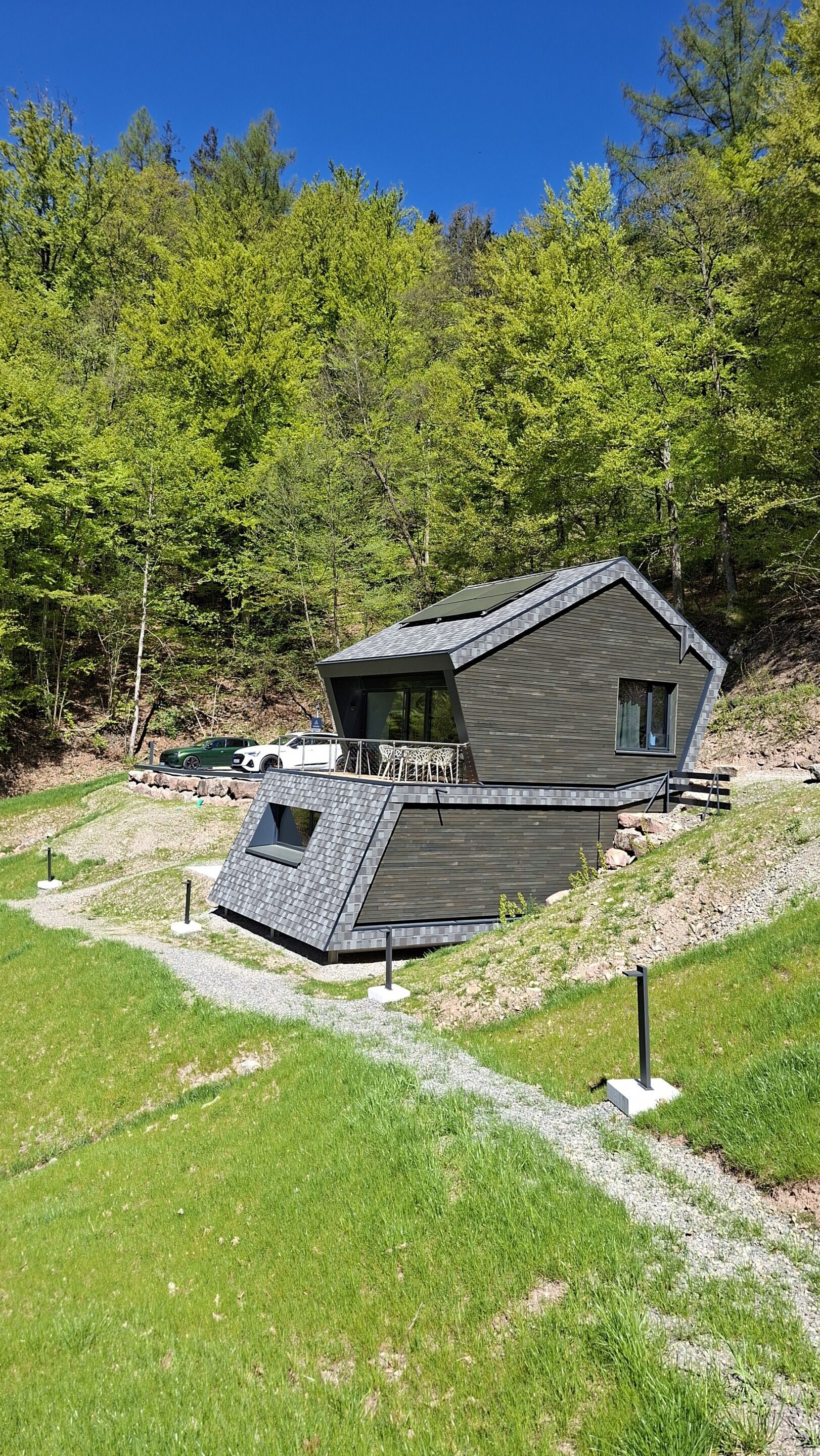 Une maison moderne avec un toit en pente, un balcon et une allée menant à l’entrée.