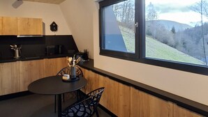 A modern kitchen with wooden cabinets, a round dining table, and a window with a view of a hillside. - SMART LODGES (Bad Rippoldsau-Schapbach)