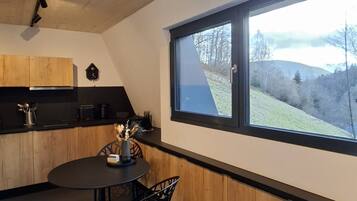 A modern kitchen with wooden cabinets, a round dining table, and a window with a view of a hillside.