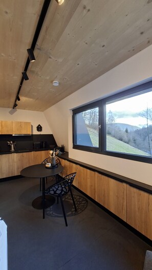A modern kitchen with wooden cabinets, a round dining table, and a window with a view of a hillside.