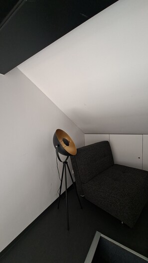 A corner of a room with a dark grey sofa, a floor lamp with a gold-colored shade, and a white wall. - SMART LODGES (Bad Rippoldsau-Schapbach)