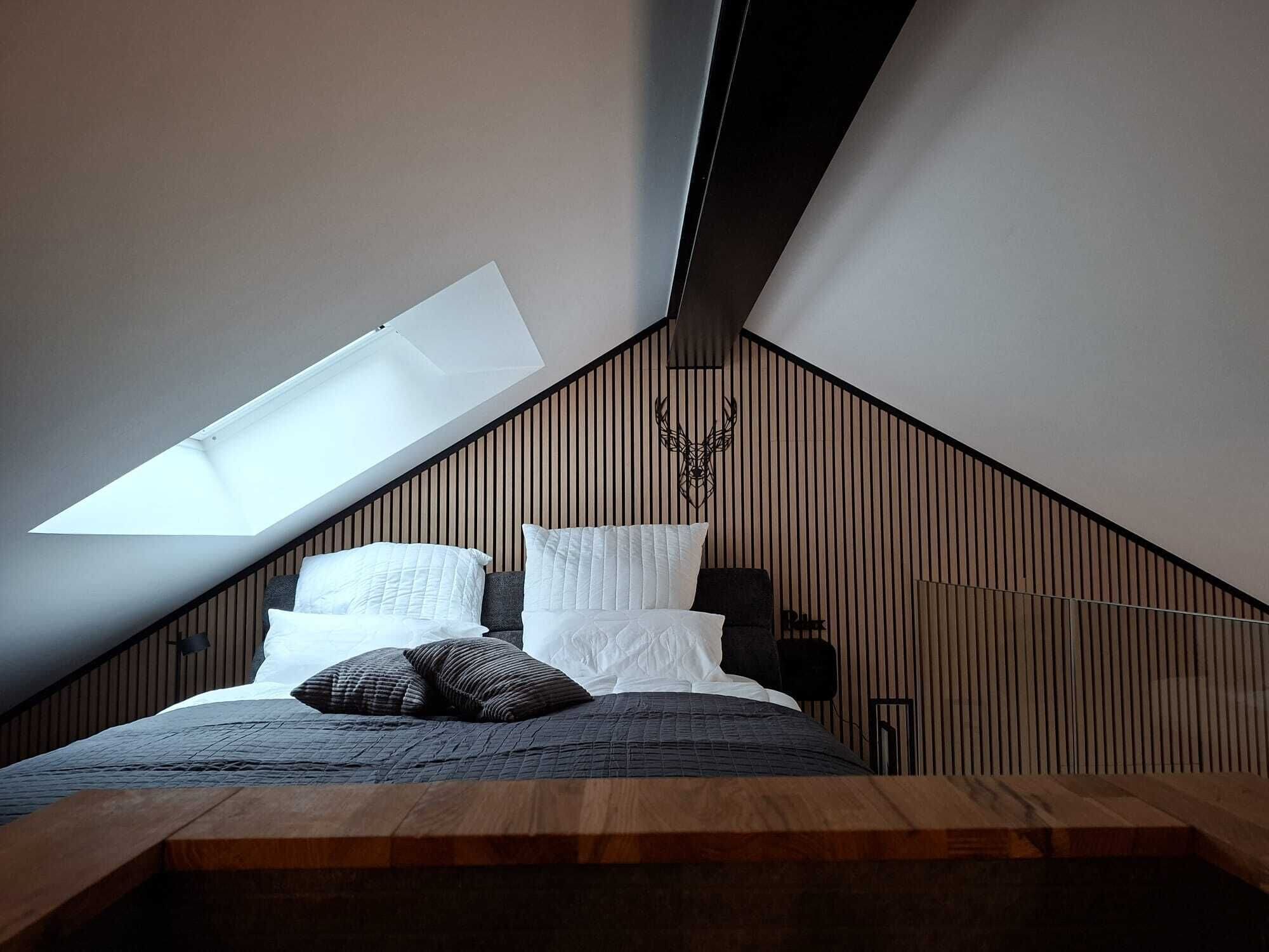 Een slaapkamer met een schuine kap, dakraam, een bed met kussens en een houten wandpaneel.