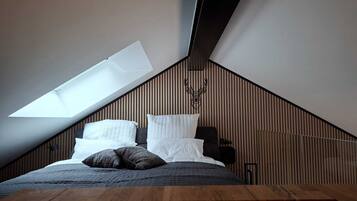 Een slaapkamer met een schuine kap, dakraam, een bed met kussens en een houten wandpaneel.