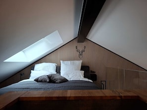 Un dormitorio con techo inclinado, tragaluces, cama con almohadas y panel de pared de madera.