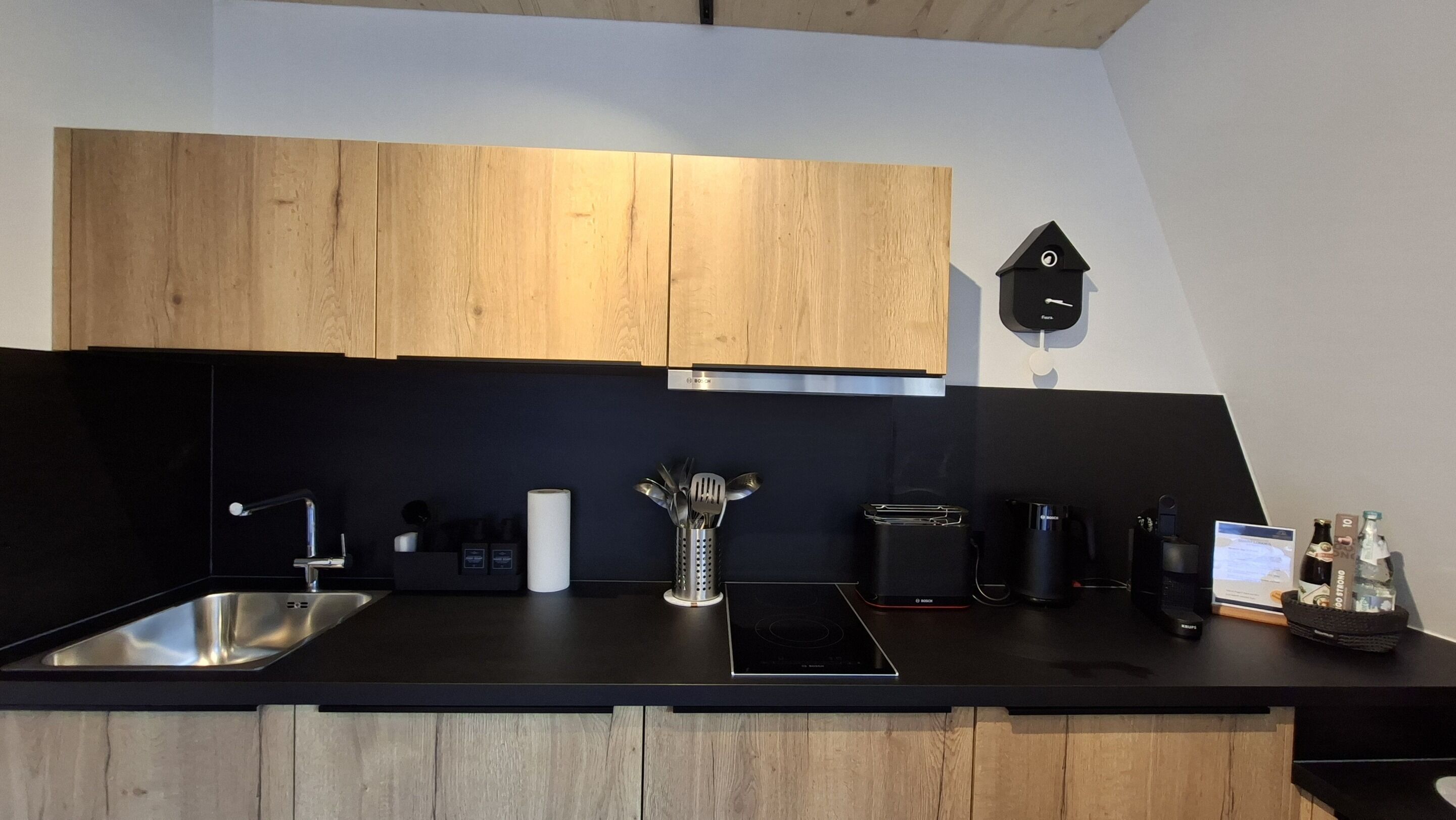 Una cocina moderna con armarios de madera, un lavamanos de acero inoxidable, una cocina de inducción Bosch y un reloj de pared.