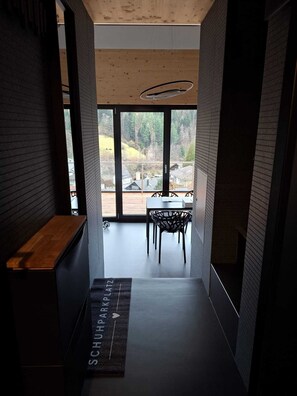 A modern interior with a wooden ceiling, a black bench, and a view of a balcony with a dining table and chairs. - SMART LODGES (Bad Rippoldsau-Schapbach)