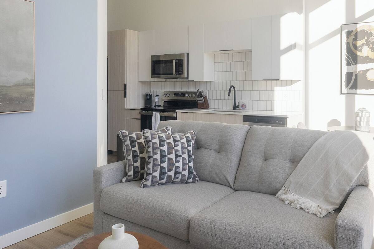 A living room with a grey sofa, a coffee table, and a kitchen in the background.