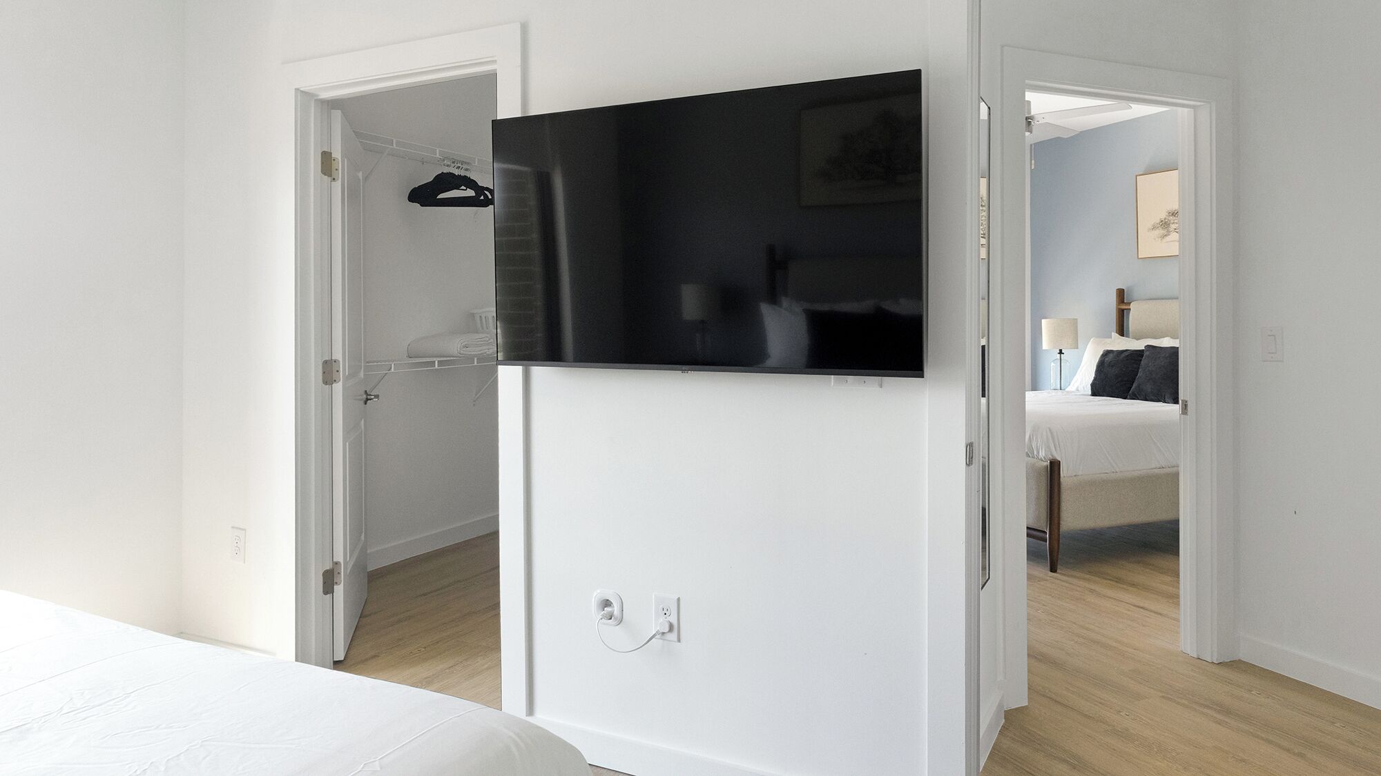 Ein Hotelzimmer mit Bett, Wandfernseher, Kleiderschrank und einem durchgehenden Tür sichtbaren Badezimmer.