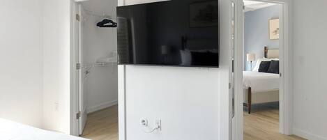 Ein Hotelzimmer mit Bett, Wandfernseher, Kleiderschrank und einem durchgehenden Tür sichtbaren Badezimmer.