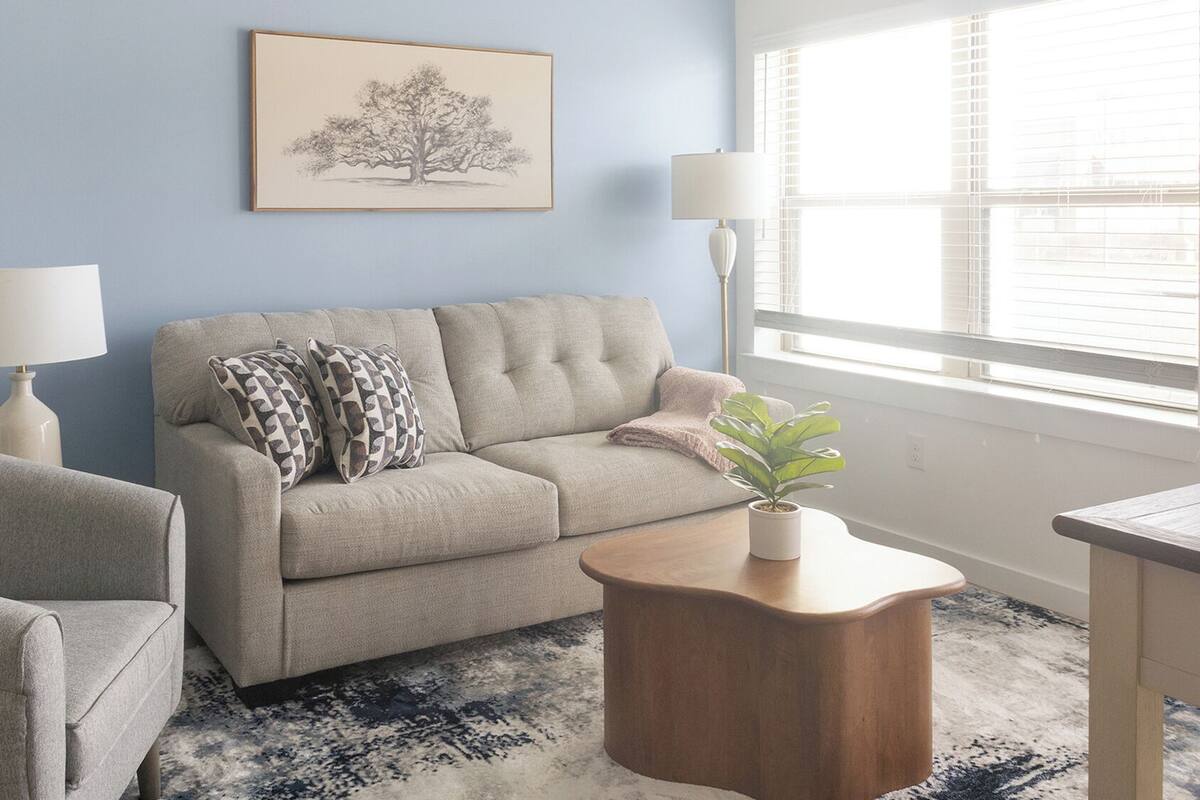 A living room with a sofa, armchair, a side table with a plant, a lamp, and a framed picture on the wall.