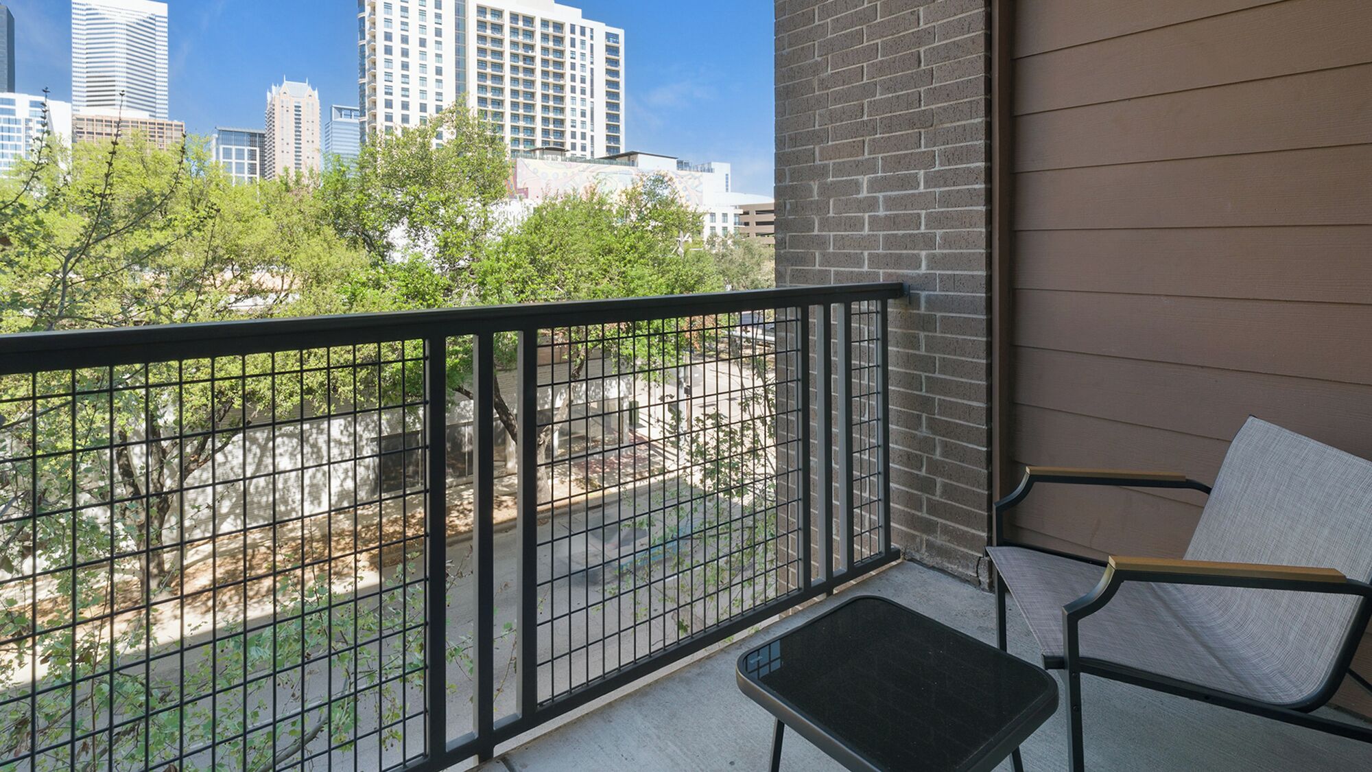 A balcony with a metal railing, a chair, and a view of a cityscape with tall buildings.