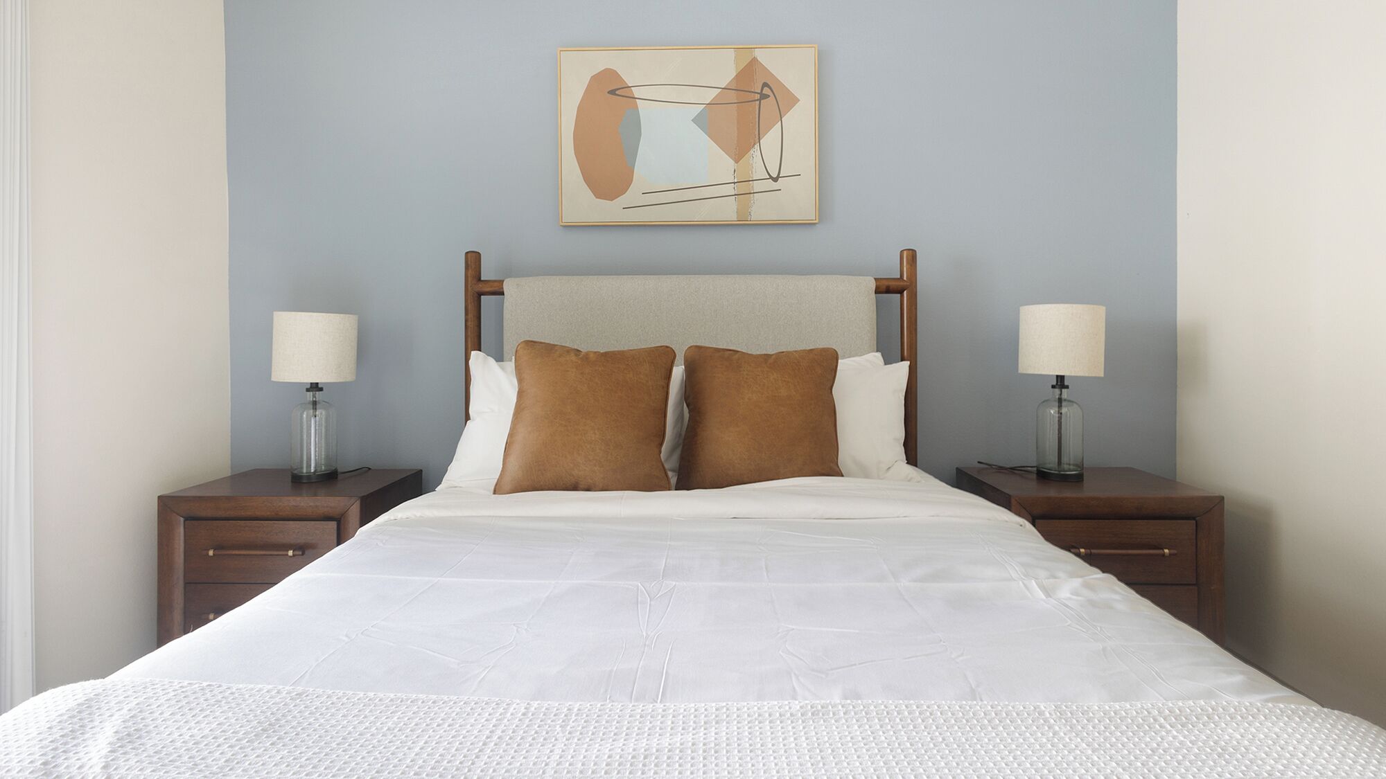 A hotel room with a bed, two nightstands, two lamps, and a wall art piece.