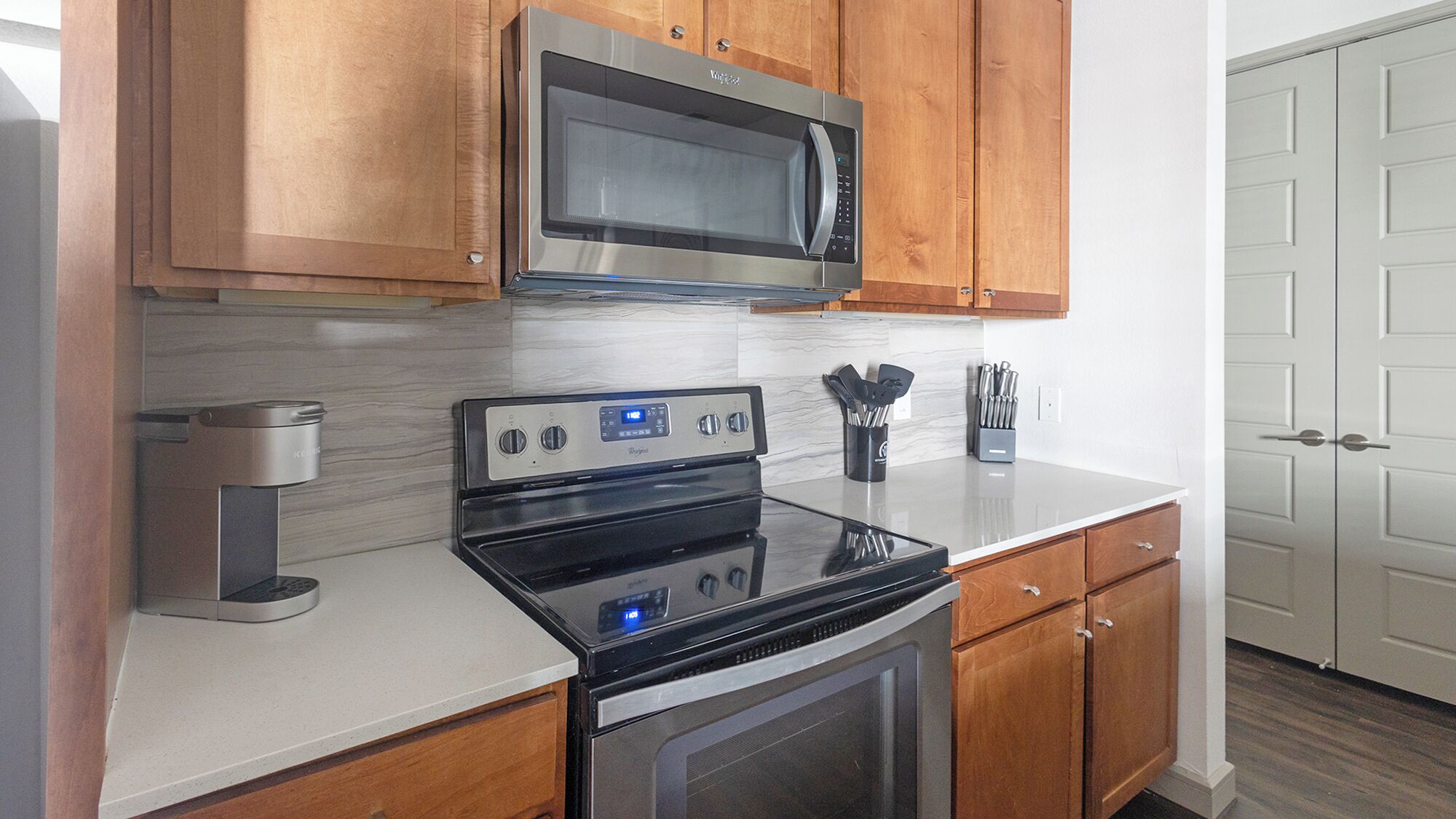 A kitchen with wooden cabinets, a stainless steel microwave, a black stove, and a coffee maker.