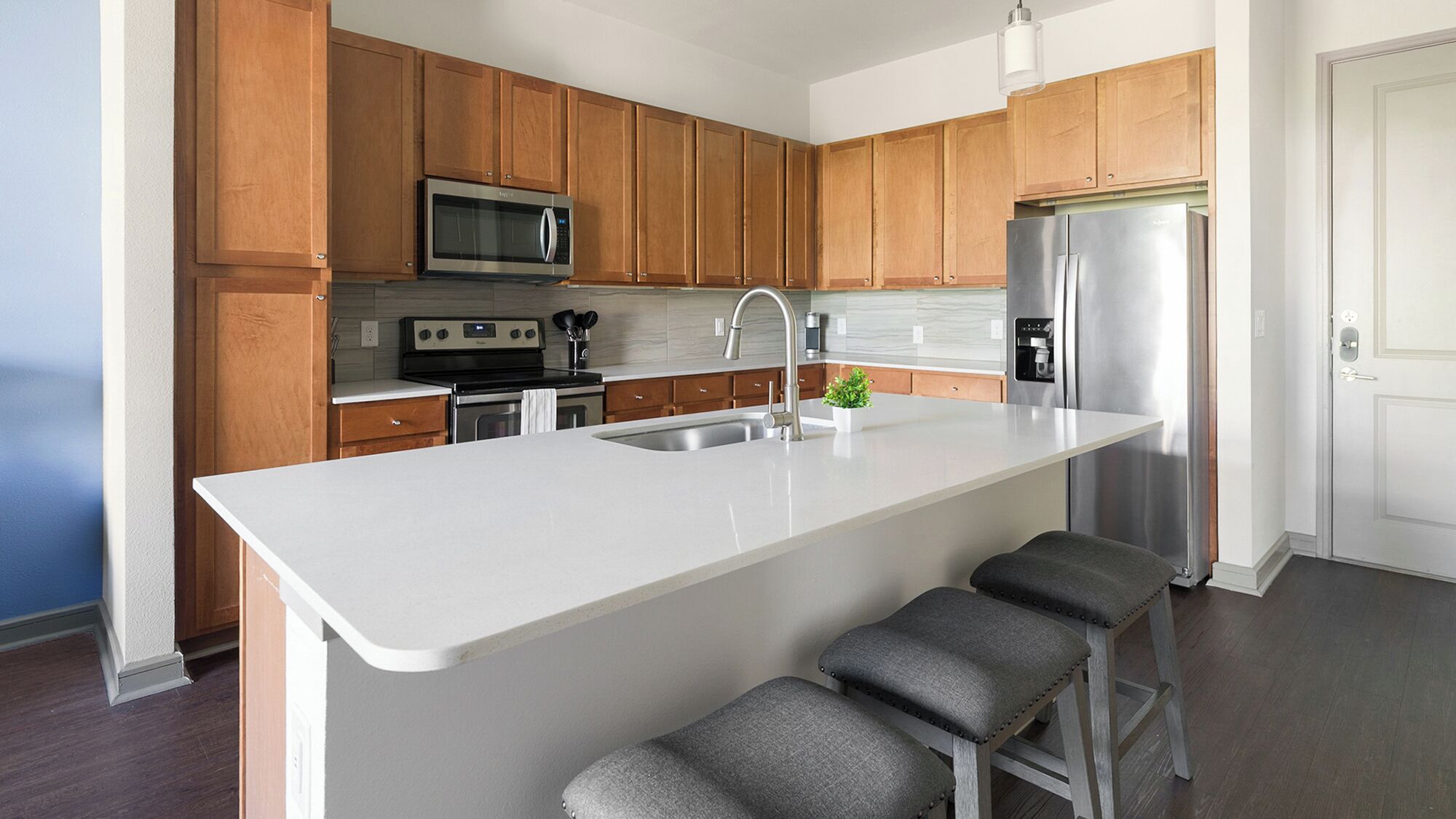 A modern kitchen with wooden cabinets, a stainless steel refrigerator, a microwave, and a sink.