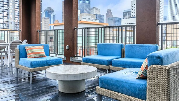 Una terrazza sul tetto con mobili in vimini, un tavolo rotondo e vista sullo skyline cittadino.