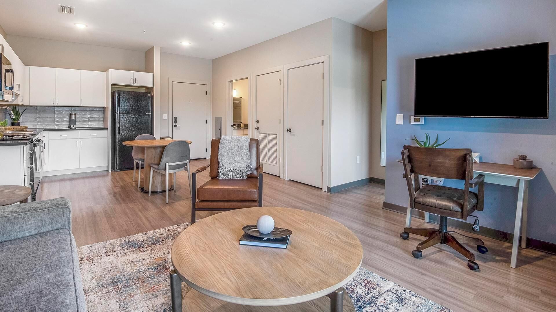 Un salon moderne avec une table basse ronde, un canapé et un téléviseur fixé au mur.