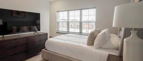 Une chambre à coucher avec un lit, une commode, un téléviseur et une fenêtre avec des stores.