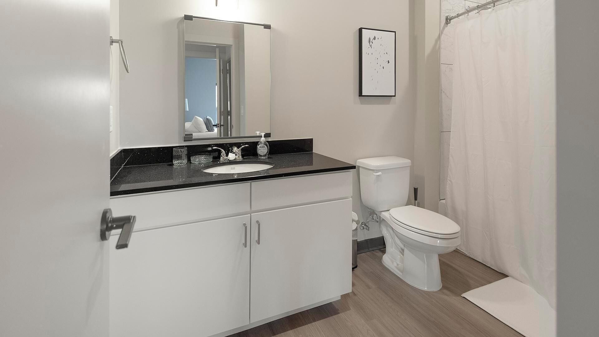 A modern bathroom with a white sink, a mirror above it, a toilet, and a shower curtain.