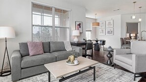 A modern living room with a grey sofa, a coffee table, and a dining area with a table and chairs. - Landing Apartments near IU Health (Indianapolis)