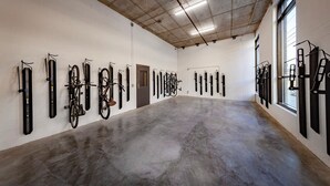A spacious indoor area with a concrete floor and white walls, featuring rows of bicycles and long black objects, possibly tools or equipment, mounted on the walls. - Landing Apartments near IU Health (Indianapolis)