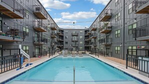 A modern building with a central swimming pool, multiple balconies, and a clear sky. - Landing Apartments near IU Health (Indianapolis)