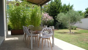 An outdoor patio with a wooden table and white chairs, surrounded by greenery and a small tree. - Holiday rental with pool in the Alpilles for 6 people (Plan-d´Orgon)