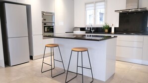 A modern kitchen with white cabinetry, a black countertop, and two wooden stools. - Holiday rental with pool in the Alpilles for 6 people (Plan-d´Orgon)