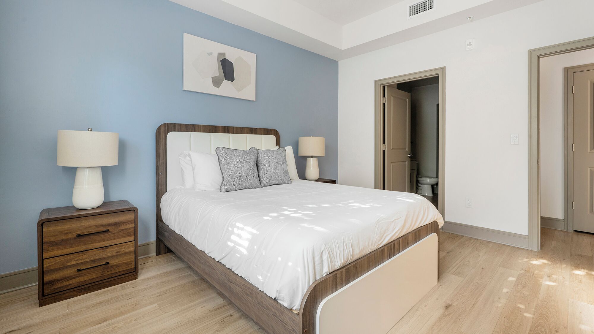 Een slaapkamer met een bed, nachtkastjes, een wandlamp en een deur naar een badkamer.