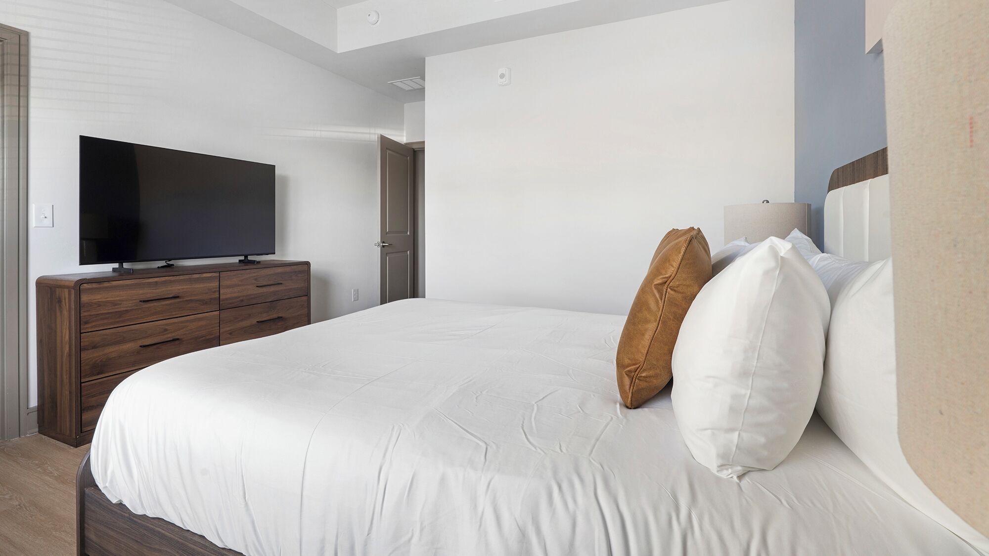 Een slaapkamer met een bed, een televisie op een houten dressoir en een deur.