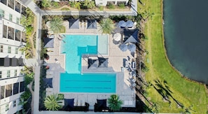 Vista aérea de un hotel con una amplia piscina central, numerosas tumbonas y un jardín circundante con palmeras.
