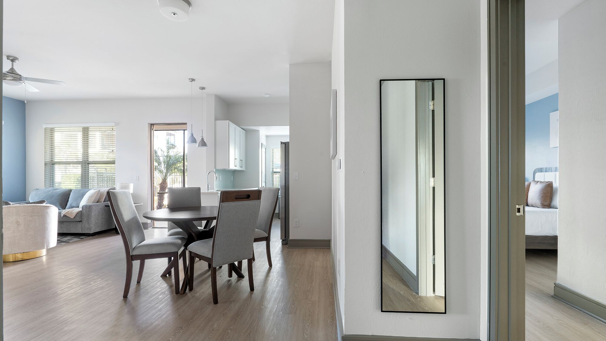 A modern living room with a dining area, a kitchen, and a bedroom visible through an open door.