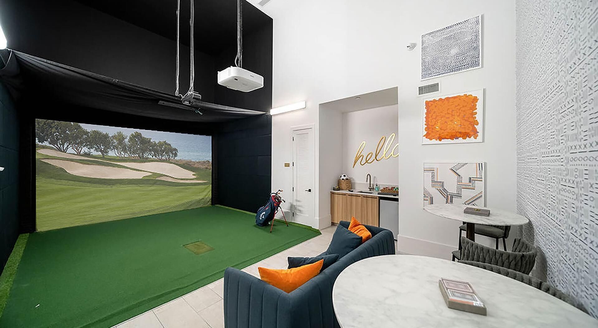 Una habitació amb un simulador de golf, una zona d'estar acollidora i una cuina.