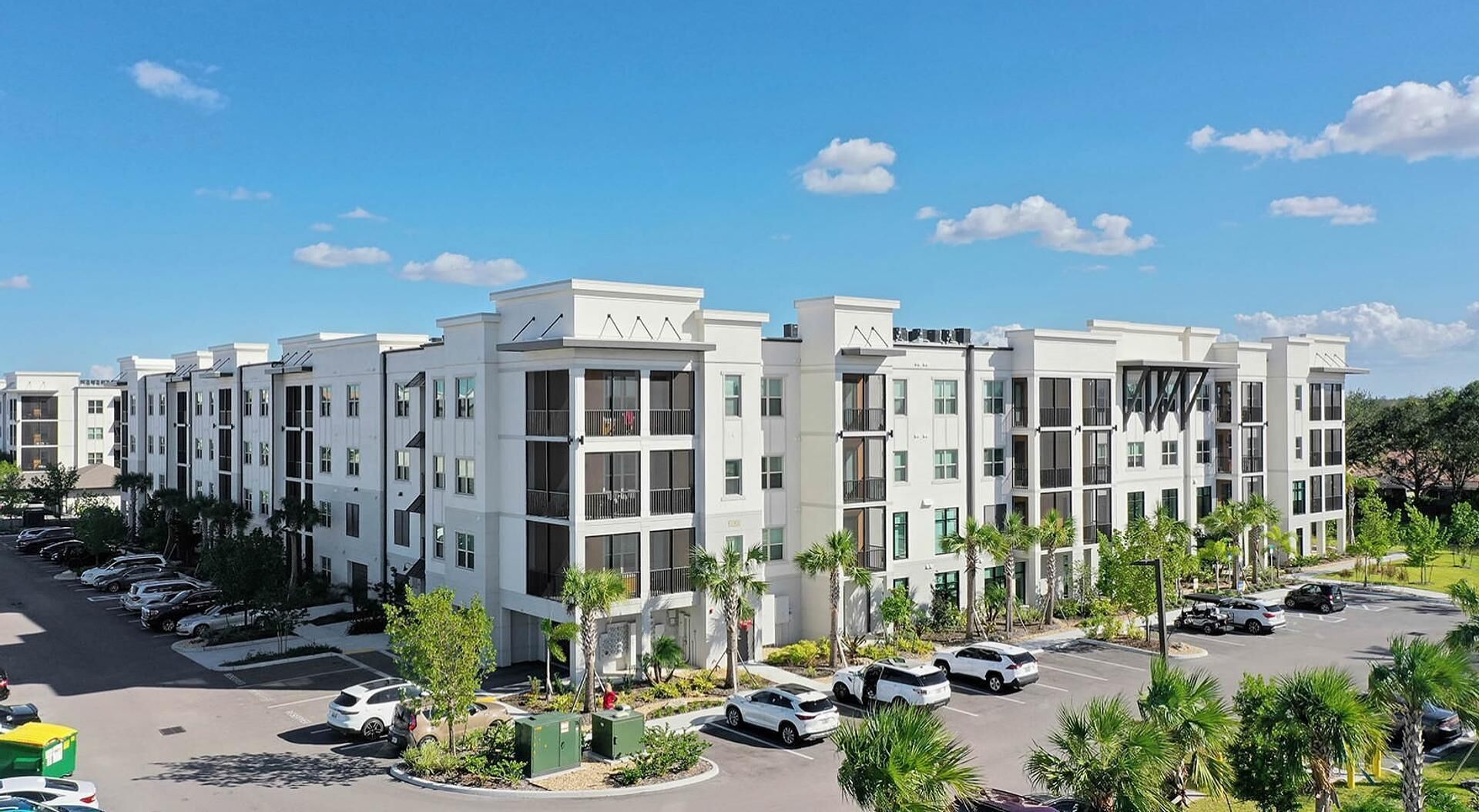 A modern multi-story residential building with a parking lot and landscaped areas.