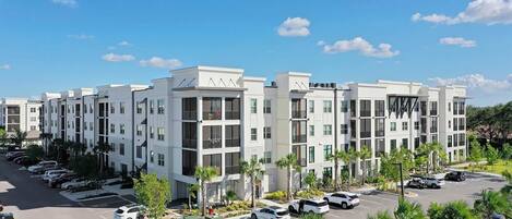 A modern multi-story residential building with a parking lot and landscaped areas.