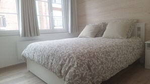 A bedroom with a bed, a window with curtains, and a wooden floor.