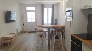 A compact kitchen with a wooden table, bar stools, a microwave, and a refrigerator.