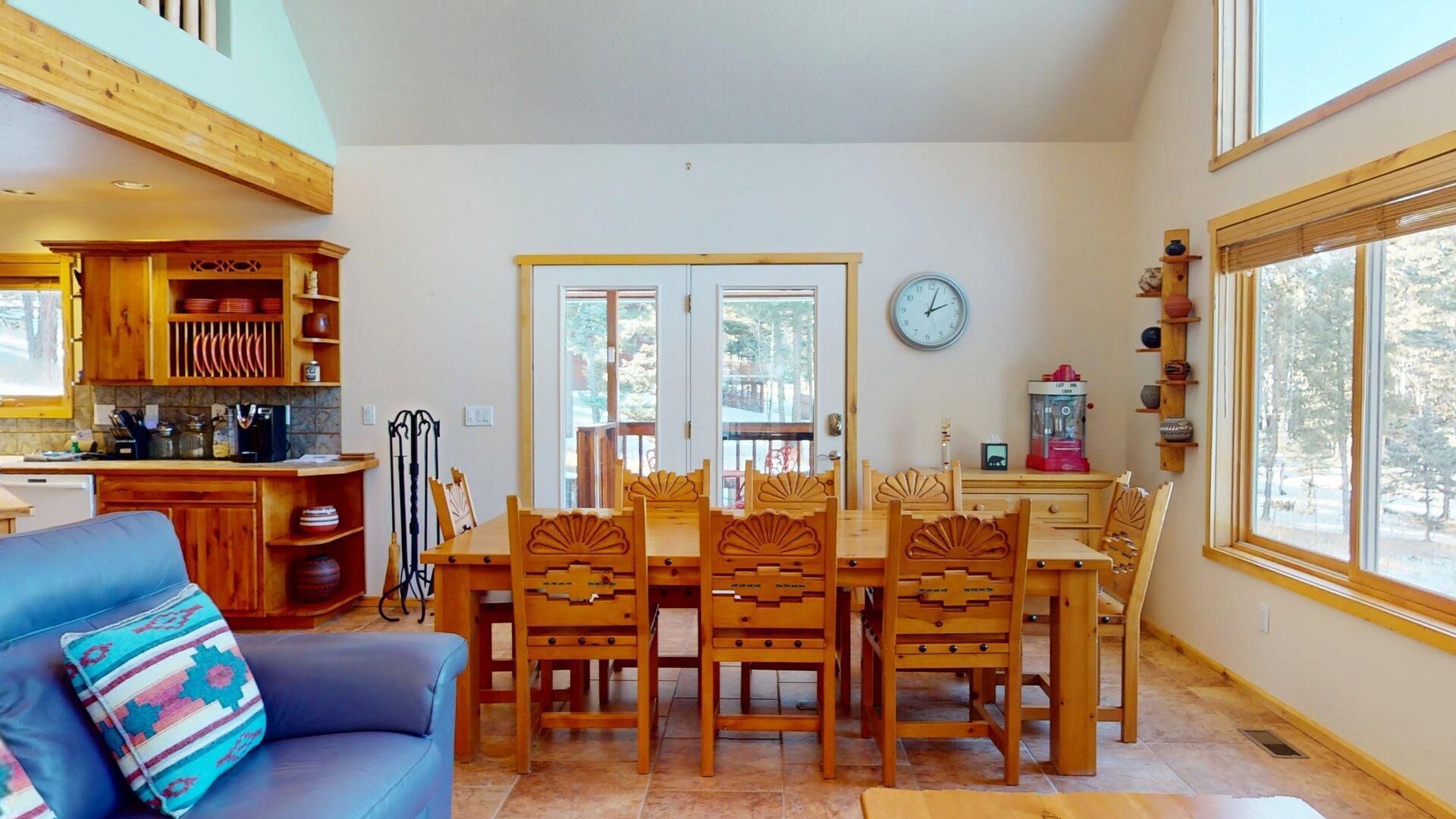 A cozy dining area with wooden furniture, a clock on the wall, and a view of the outdoors through large windows.
