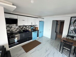 Eine moderne Küche mit schwarzen und weißen Schränken, einem blauen Kühlschrank und einem Essbereich mit Tisch und Stühlen.