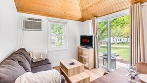 Una sala de estar acogedora con techo de madera, un televisor, un sofá, una mesa de centro y una mesa de comedor con cubierta de vidrio.