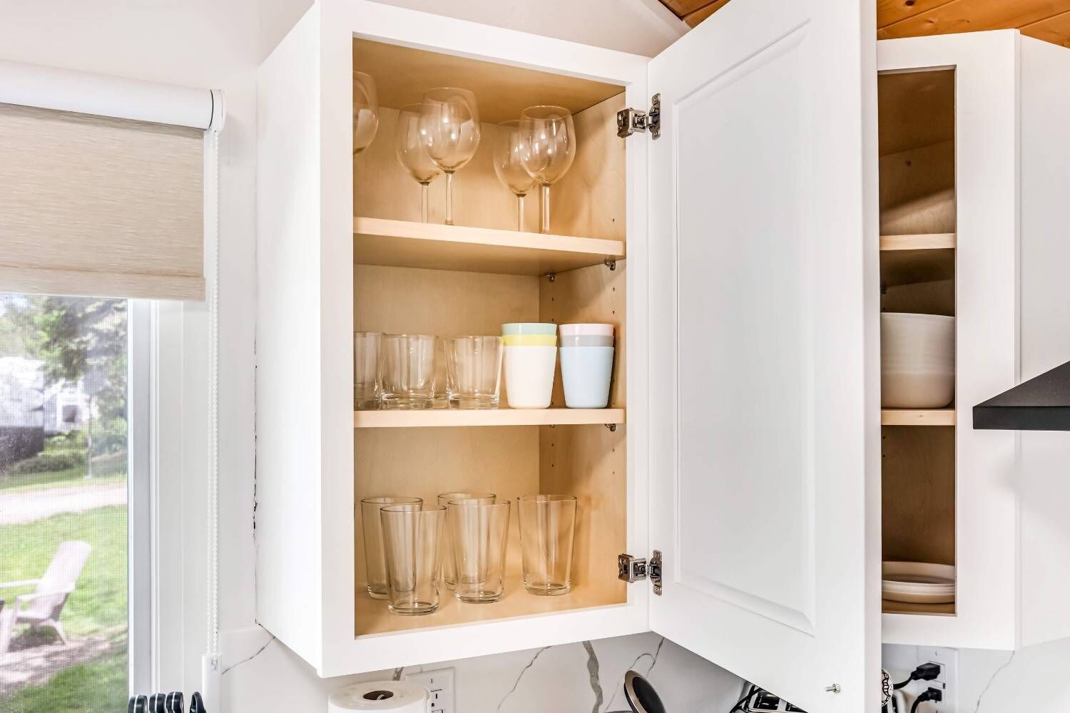 Un meuble de cuisine doté d’étagères où sont rangés des verres à vin, des tasses et des bols.