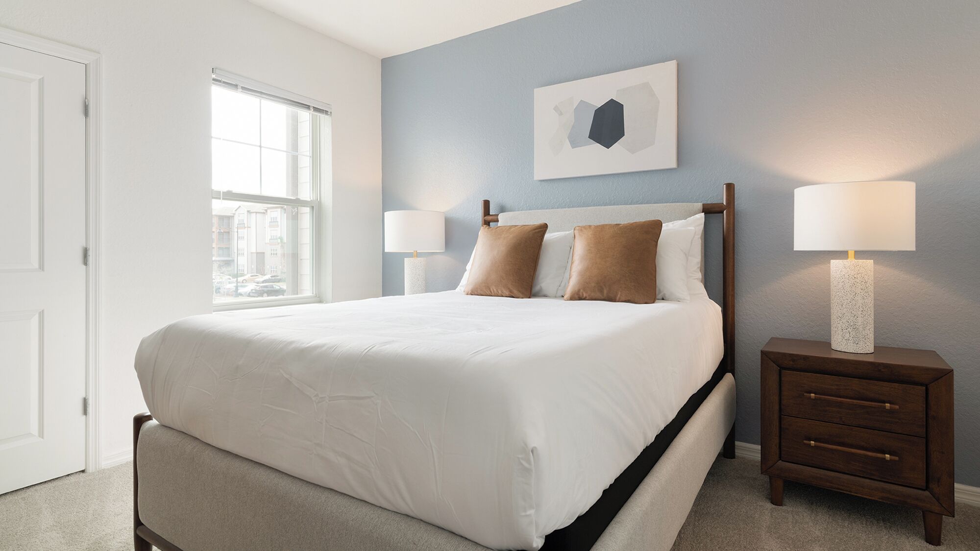 A bedroom with a bed, two bedside tables, a window, and a wall-mounted artwork.