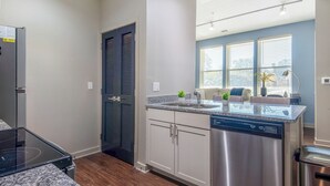 Una cucina moderna con lavastoviglie, una porta a due ante e una finestra che si affaccia su un soggiorno.
