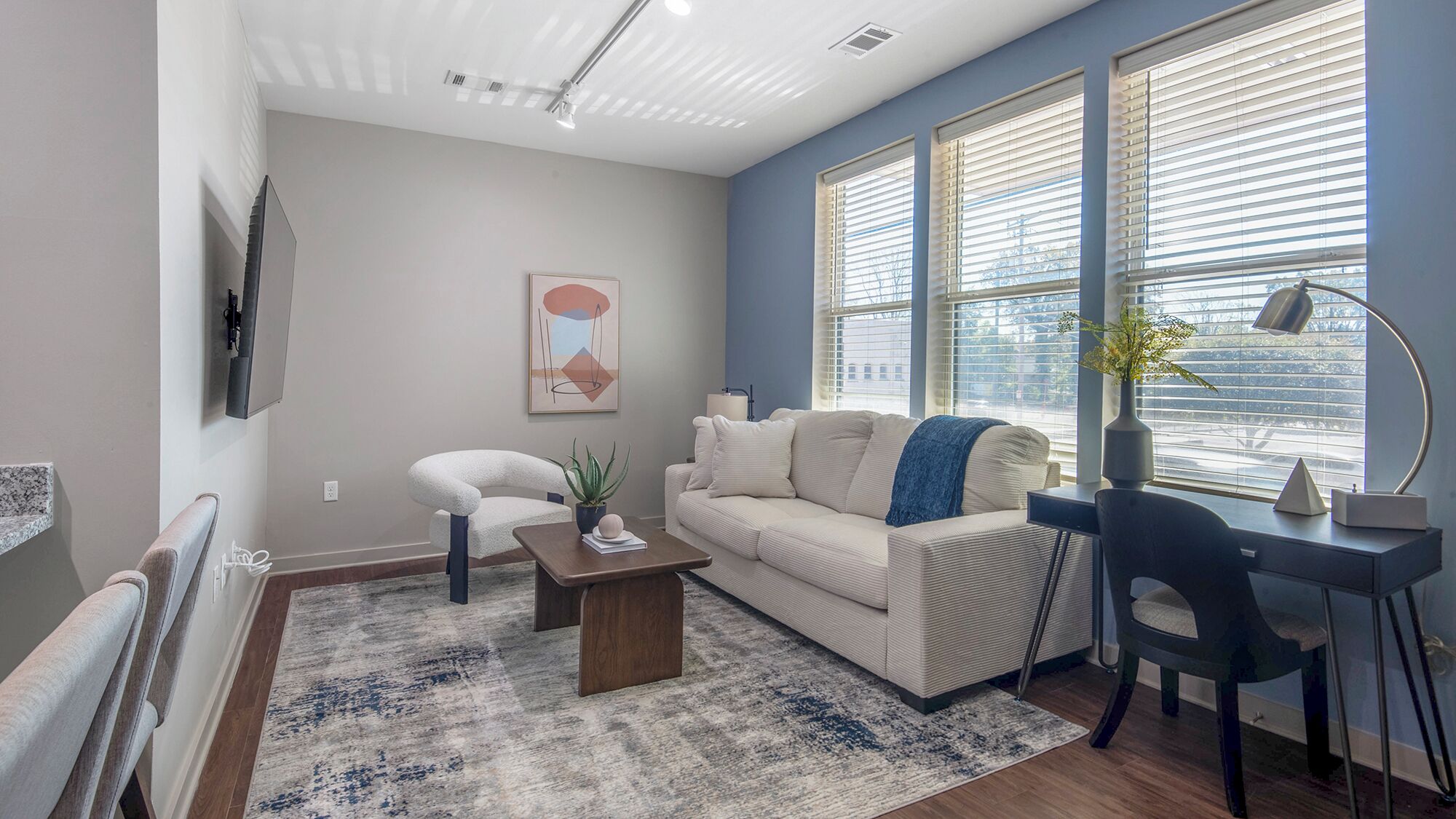 A modern living room with a sofa, a coffee table, a desk with a chair, and a TV mounted on the wall.