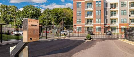 A multi-story apartment building with a brick facade, multiple balconies, and a gated parking area.